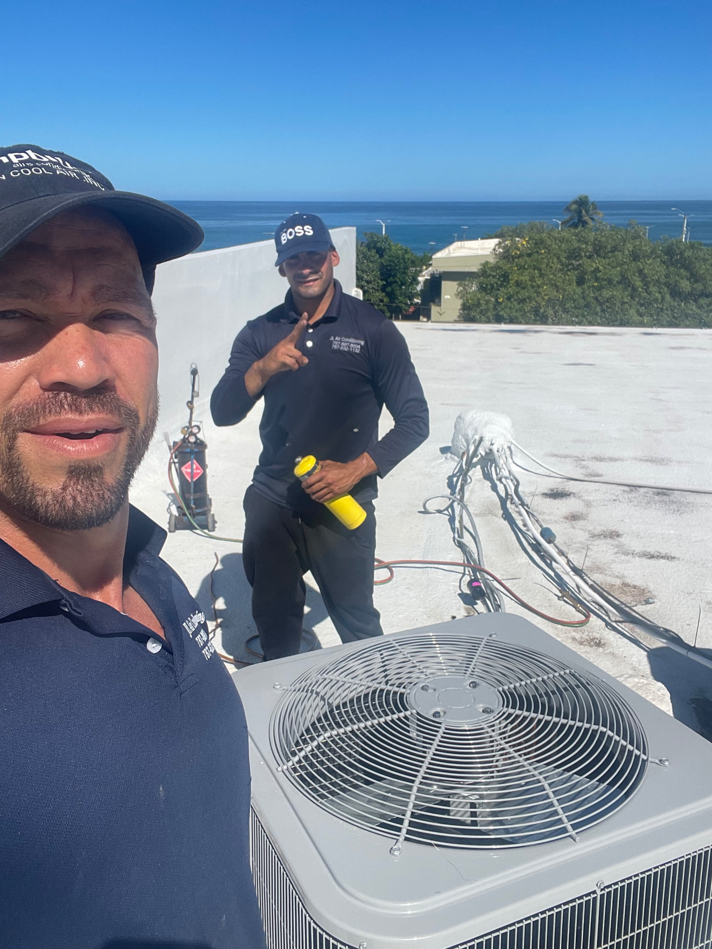 Dos técnicos de JL en una azotea junto a un equipo de aire acondicionado, con el mar de fondo