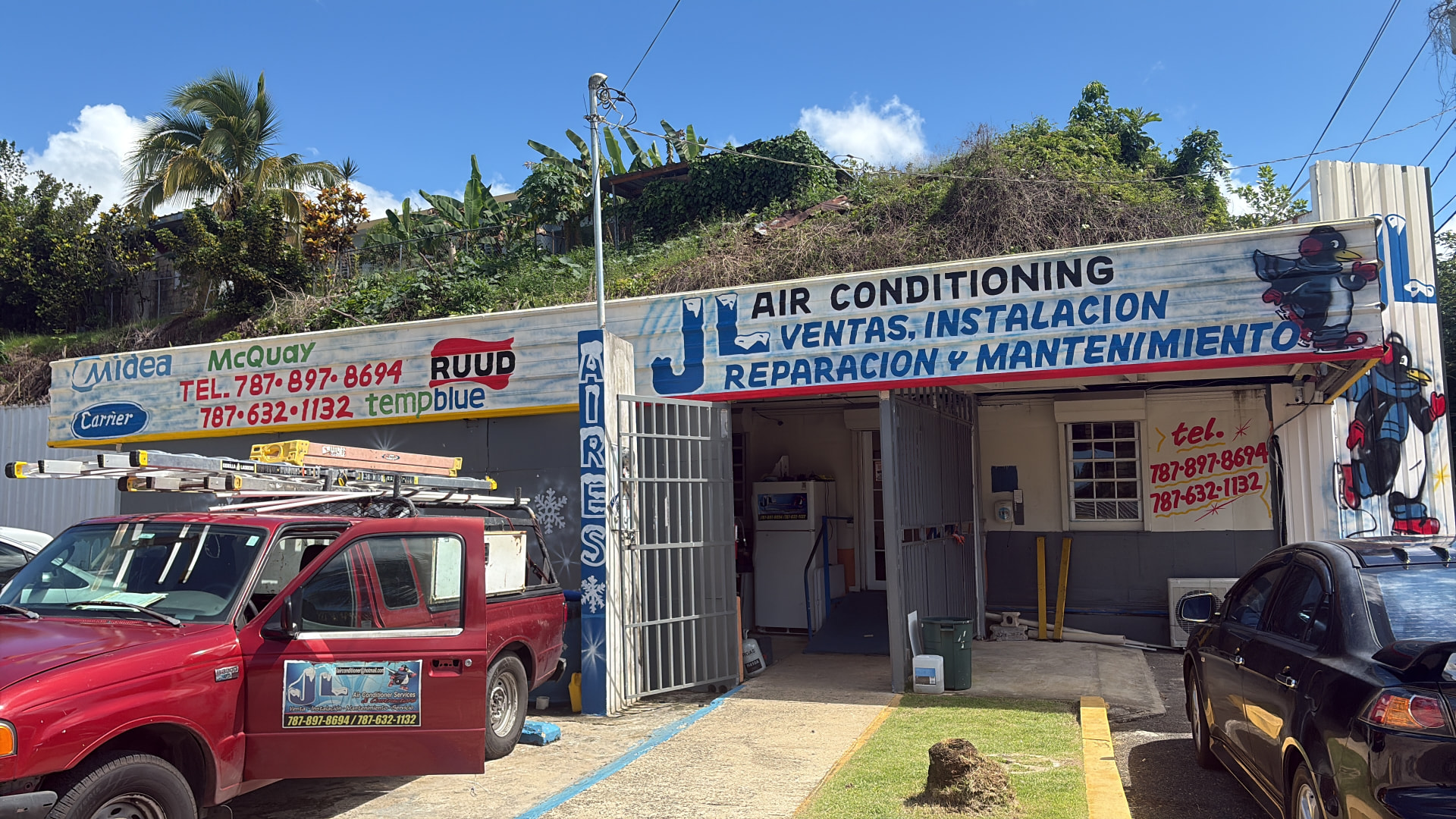 Fachada del taller de JL Air Conditioning en Lares, con letreros de marcas de aire acondicionado y los teléfonos de la oficina